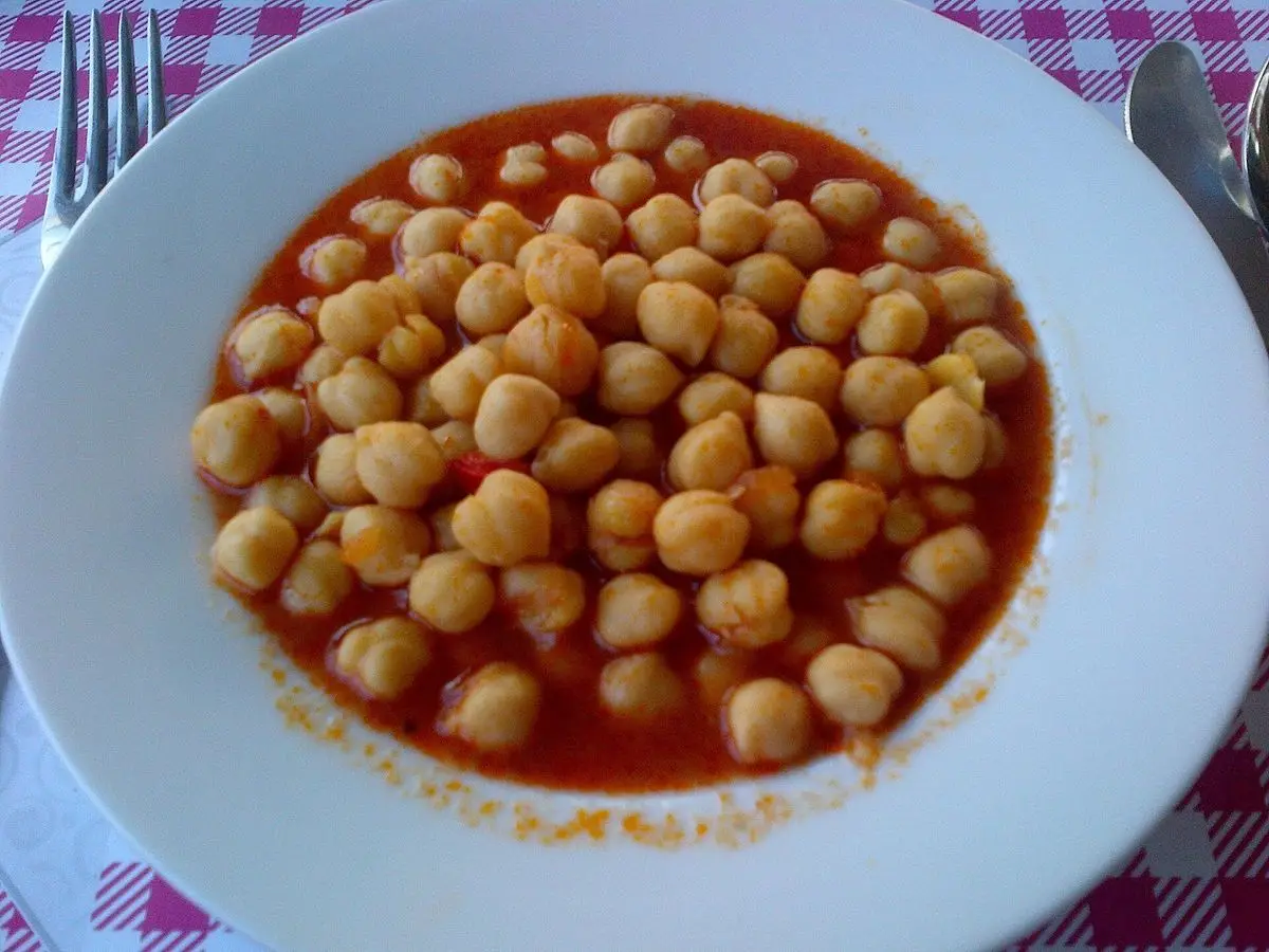 Plato blanco de garbanzos guisados en salsa de tomate sobre mantel de cuadros