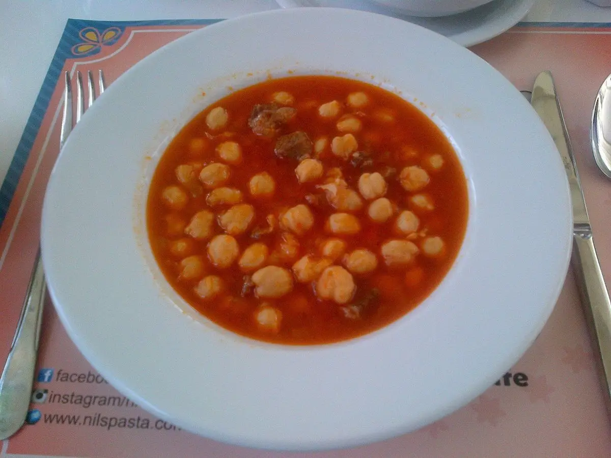 Plato blanco de garbanzos en salsa roja de tomate sobre un mantel
