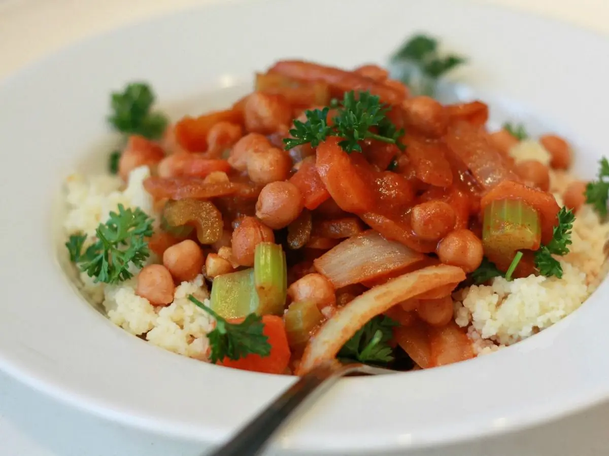 Plato de guiso de garbanzos con verduras, tomate y perejil sobre cuscús