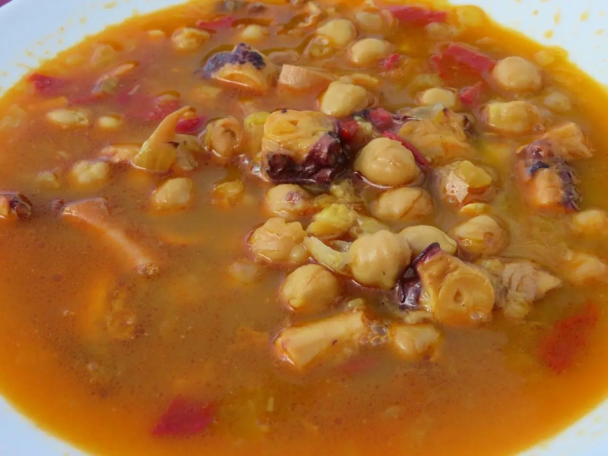 Plato hondo de potaje de garbanzos con trozos de pulpo y caldo anaranjado