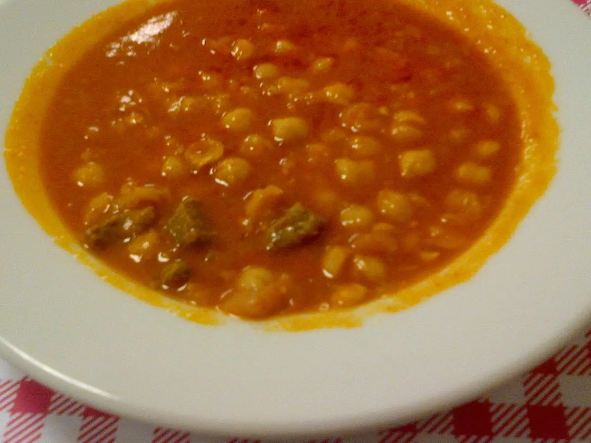 Plato de garbanzos guisados en caldo anaranjado sobre mantel de cuadros rojos