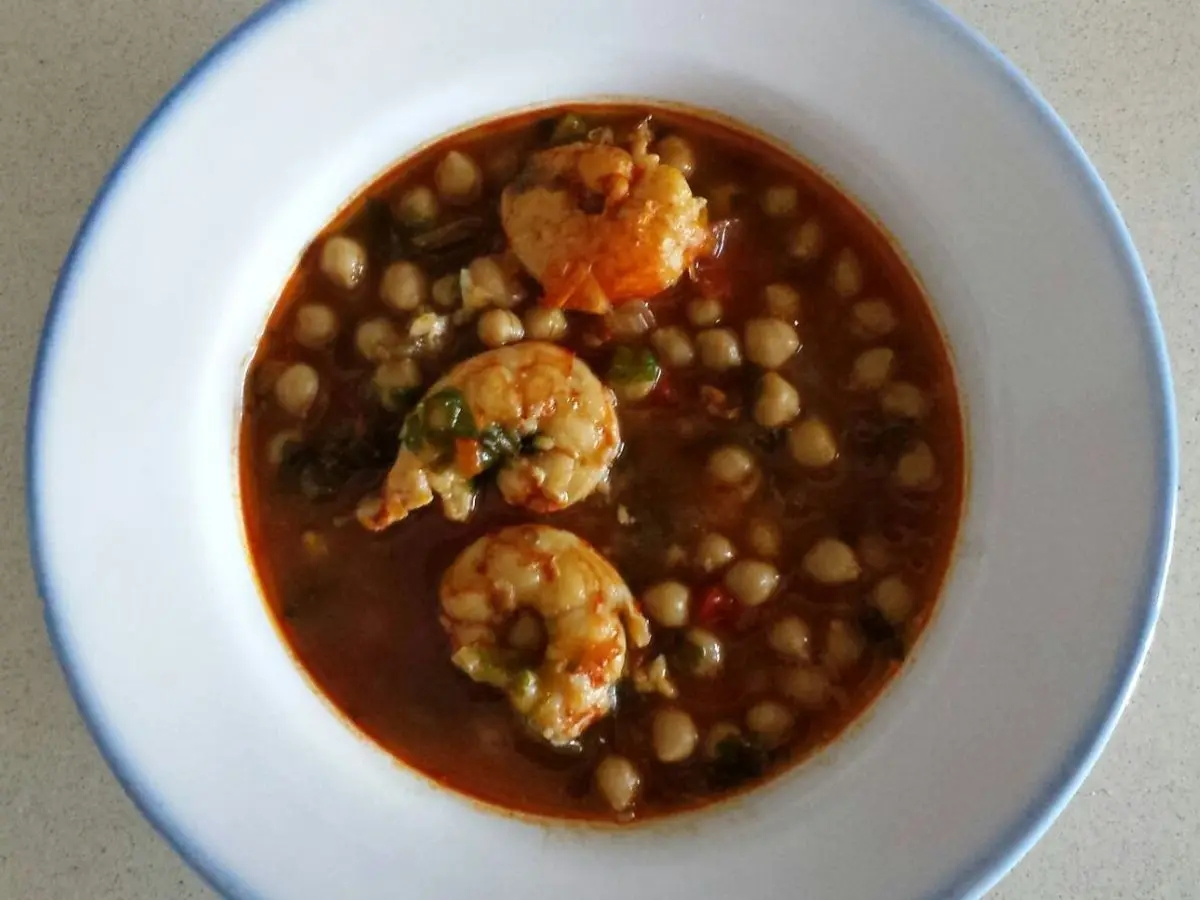 Plato hondo de garbanzos guisados con langostinos en salsa rojiza