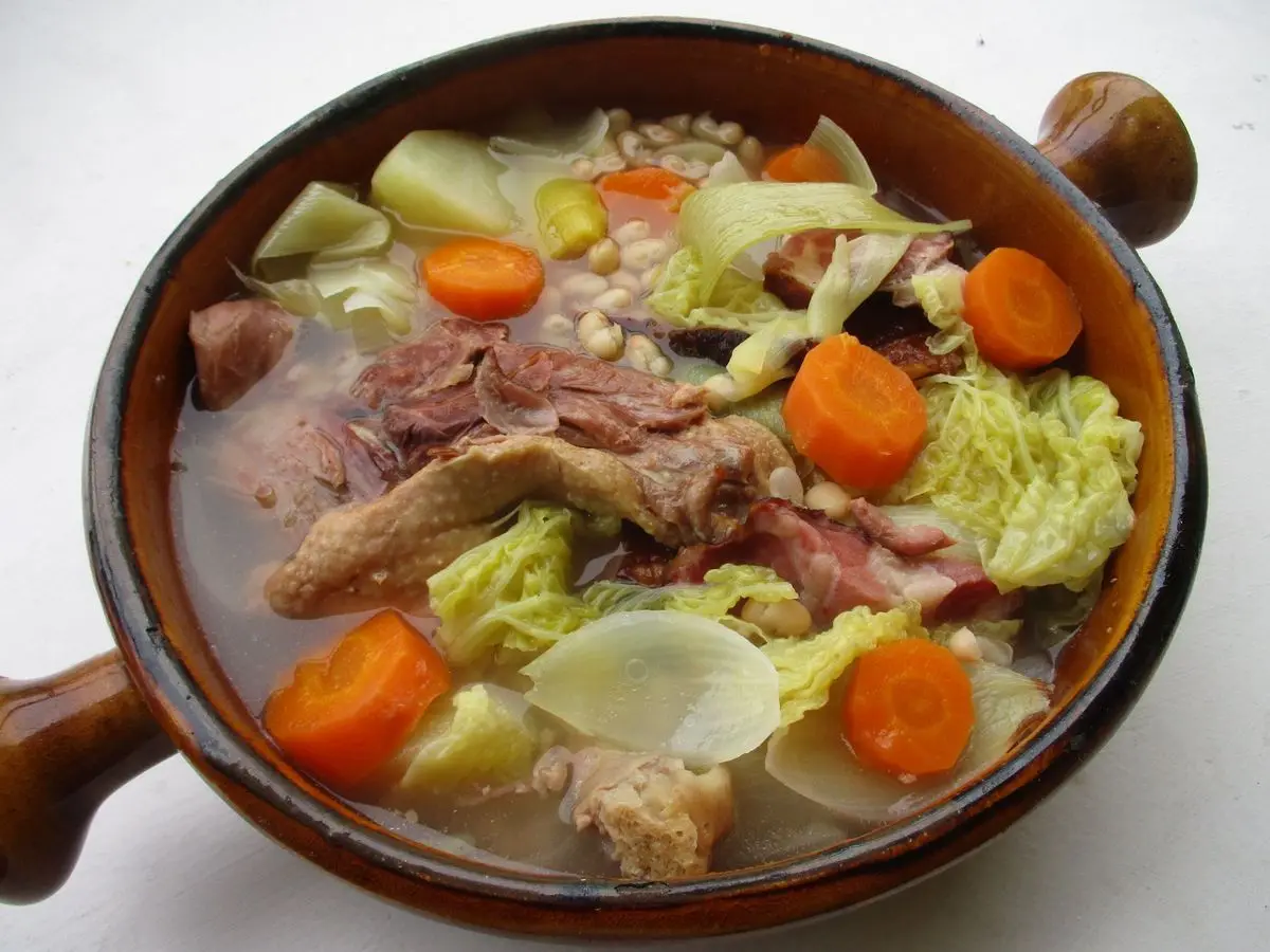 Cazuela de barro con garbure de col, zanahoria, alubias y carne de pato confitado
