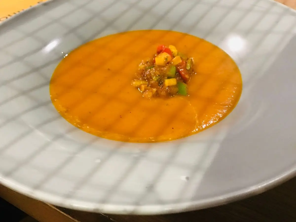 Crema de tomate anaranjada con un montoncito de verduras picadas en el centro de un plato hondo blanco