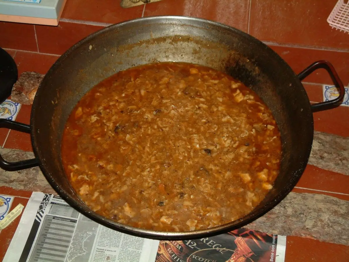 Gazpacho manchego guisado en una gran sartén de hierro, con trozos de carne y torta, sobre una mesa
