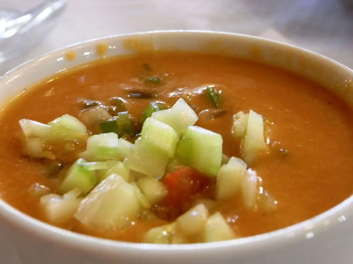 Cuenco blanco de gazpacho de tomate con dados de pepino por encima
