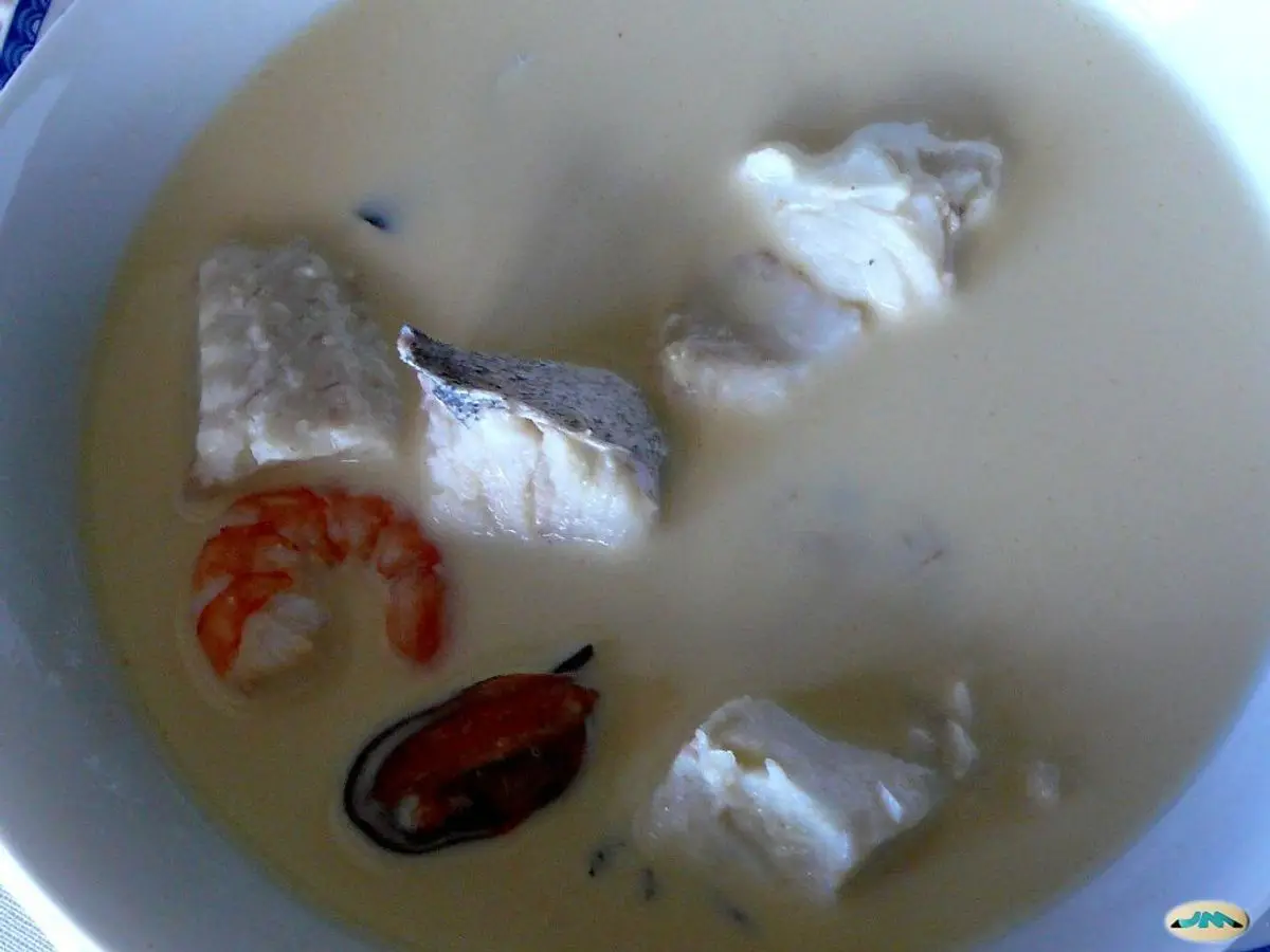 Plato hondo de sopa cremosa blanca con trozos de pescado, una gamba y un mejillón