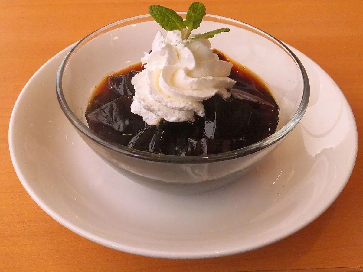 Cuenco de gelatina de café con nata montada y una hojita de menta sobre un plato blanco
