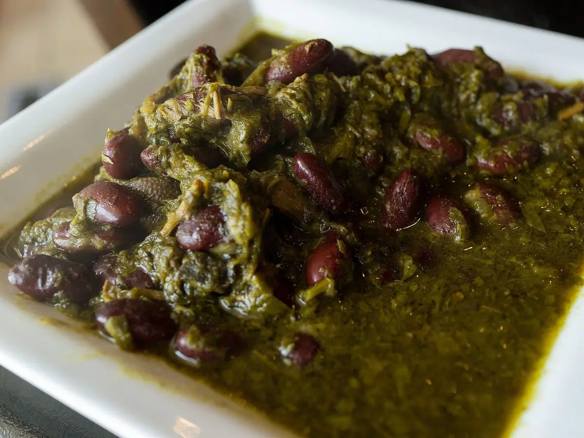 Guiso verde oscuro de hierbas con alubias rojas y carne en una fuente blanca rectangular