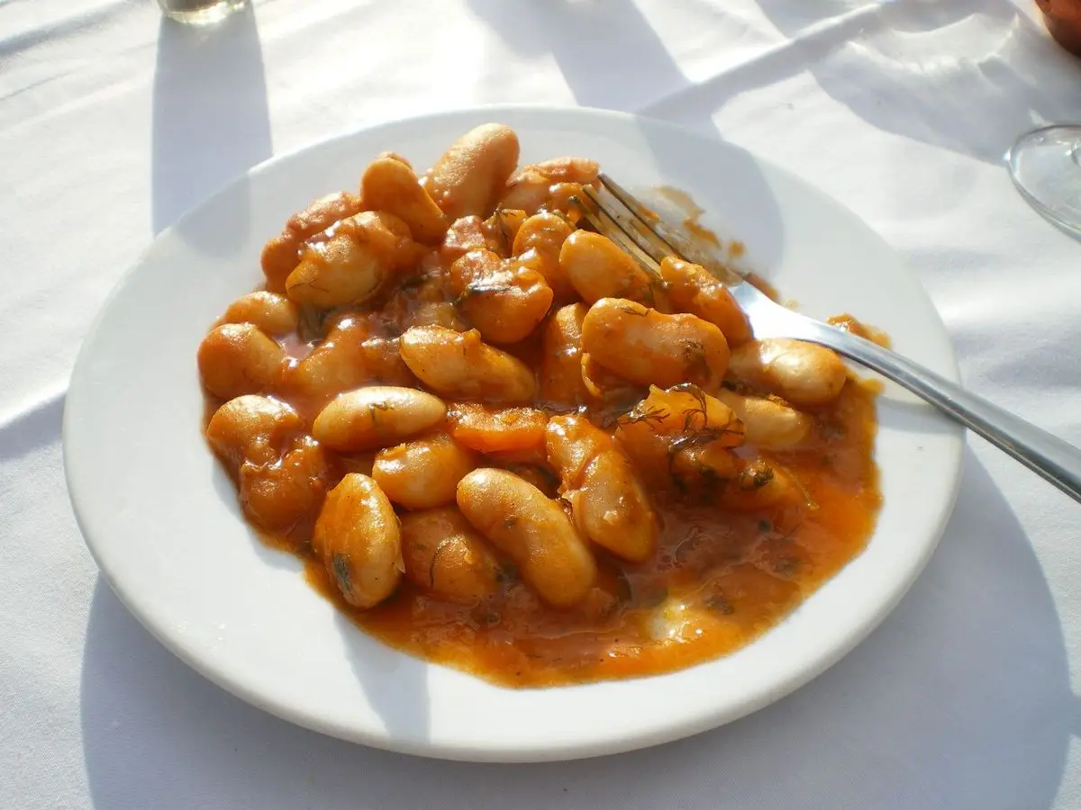 Plato blanco con alubias gigantes al horno en salsa de tomate y un tenedor