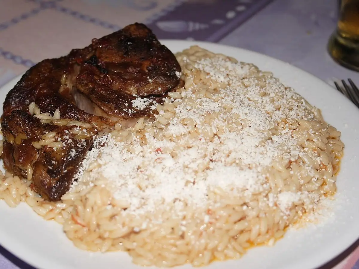 Plato blanco con carne estofada y pasta tipo arroz cubierta de queso rallado