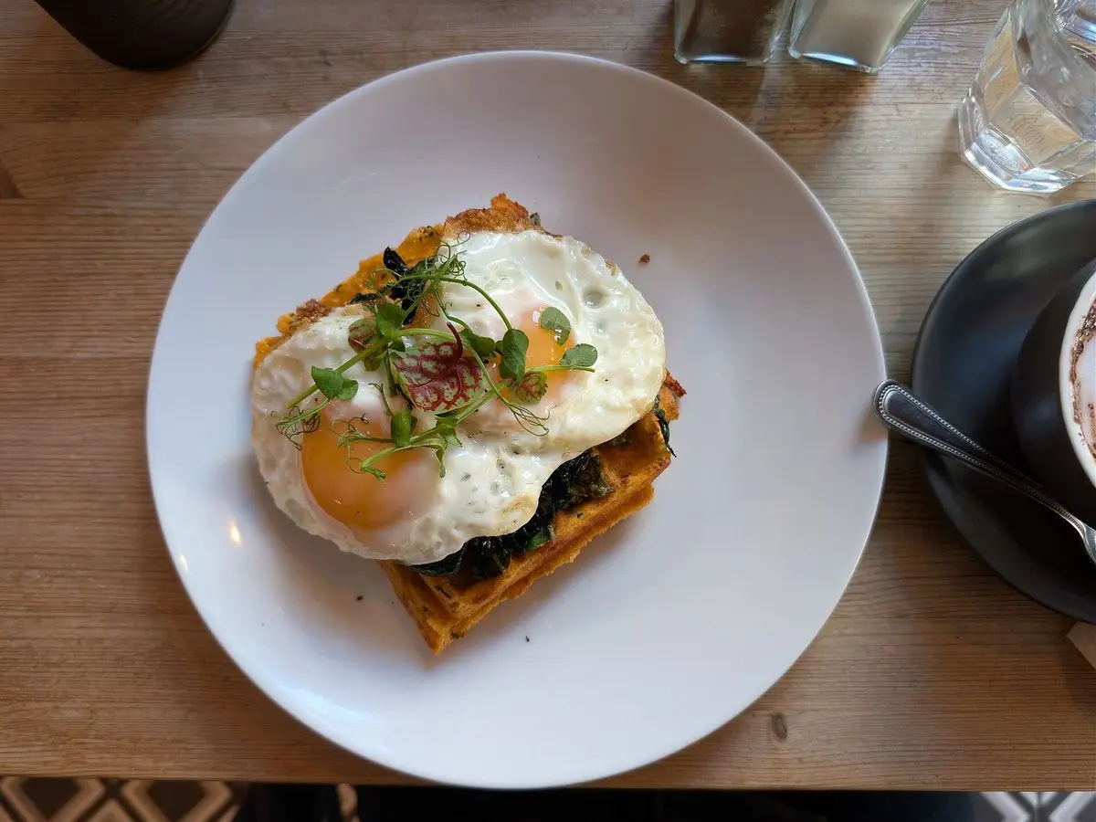 Gofre salado de queso con espinacas y dos huevos fritos con brotes verdes por encima en un plato blanco