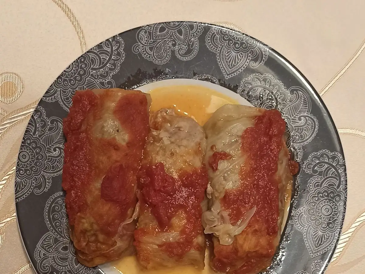 Tres rollos de hojas de col rellenos con salsa de tomate en un plato decorado