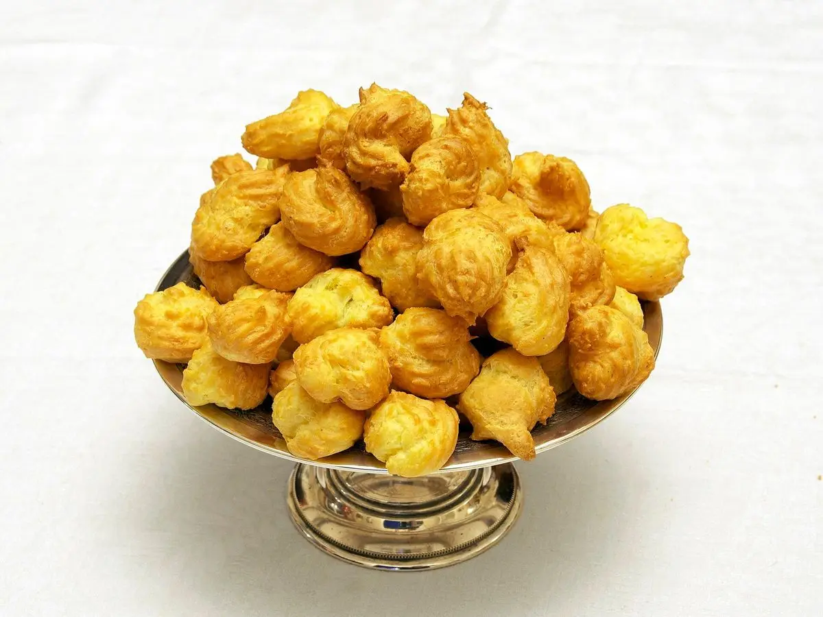 Montón de gougères, bolitas doradas de masa choux con queso, en una copa de metal sobre fondo blanco
