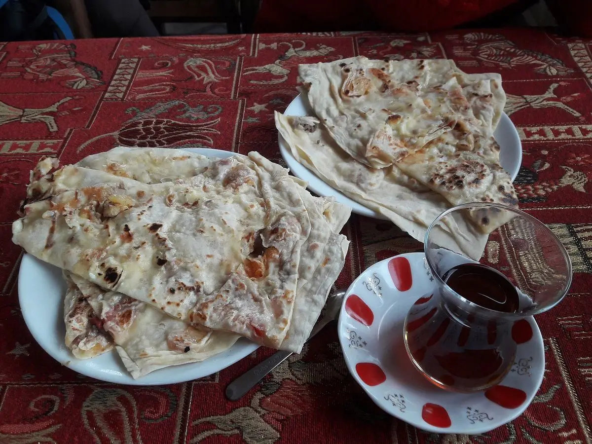 Gözleme turcos dorados y doblados sobre un plato, junto a un vaso de té sobre un mantel rojo