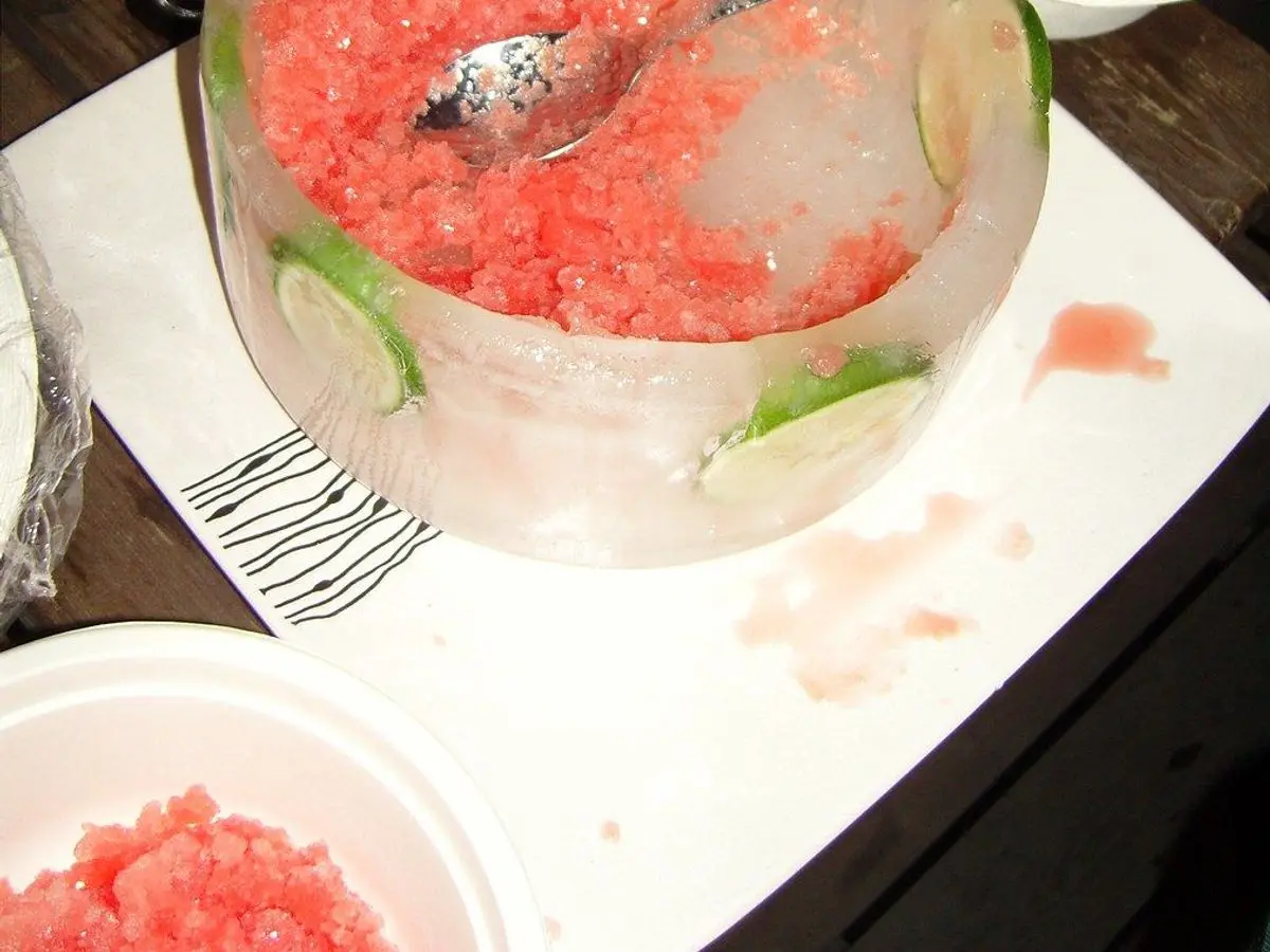 Cuenco de hielo con granizado de sandía rosado, rodajas de lima y una cuchara