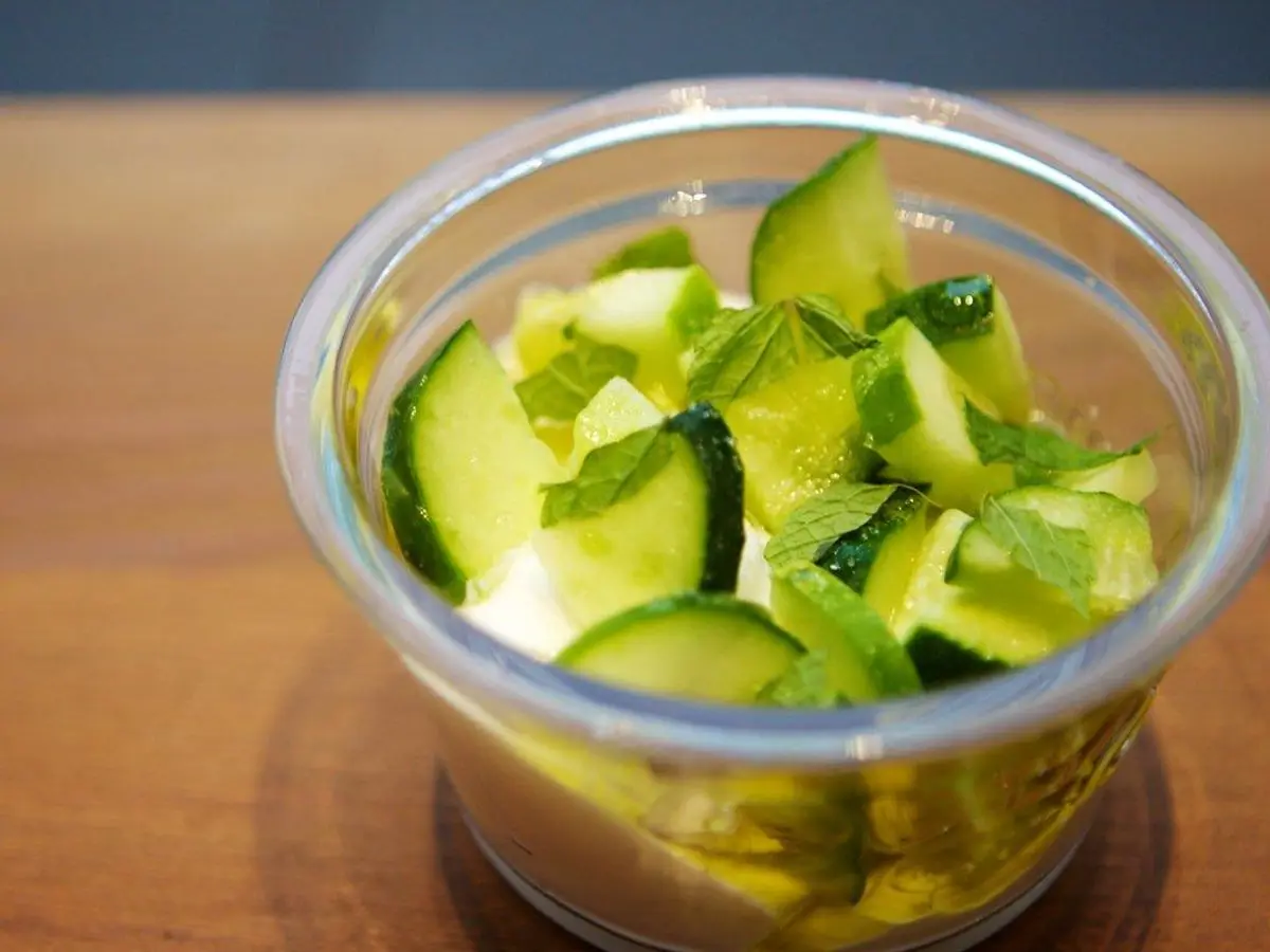 Vasito de cristal con yogur y pepino en dados con menta fresca sobre una mesa de madera