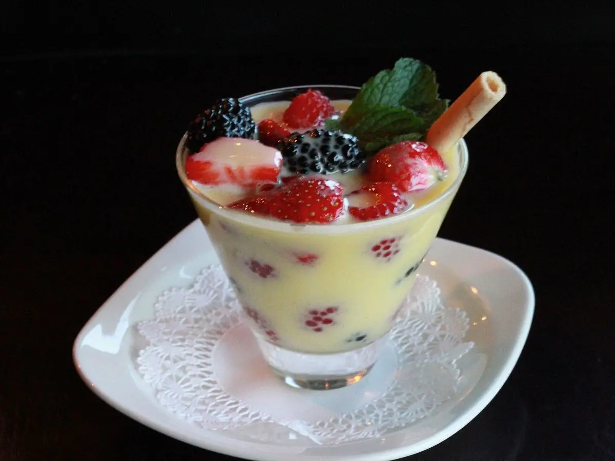 Copa de sabayón cremoso con frutos rojos y una hoja de menta, con barquillo