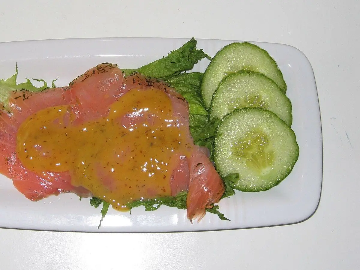 Lonchas de salmón marinado con salsa de mostaza dulce, pepino y lechuga en un plato blanco
