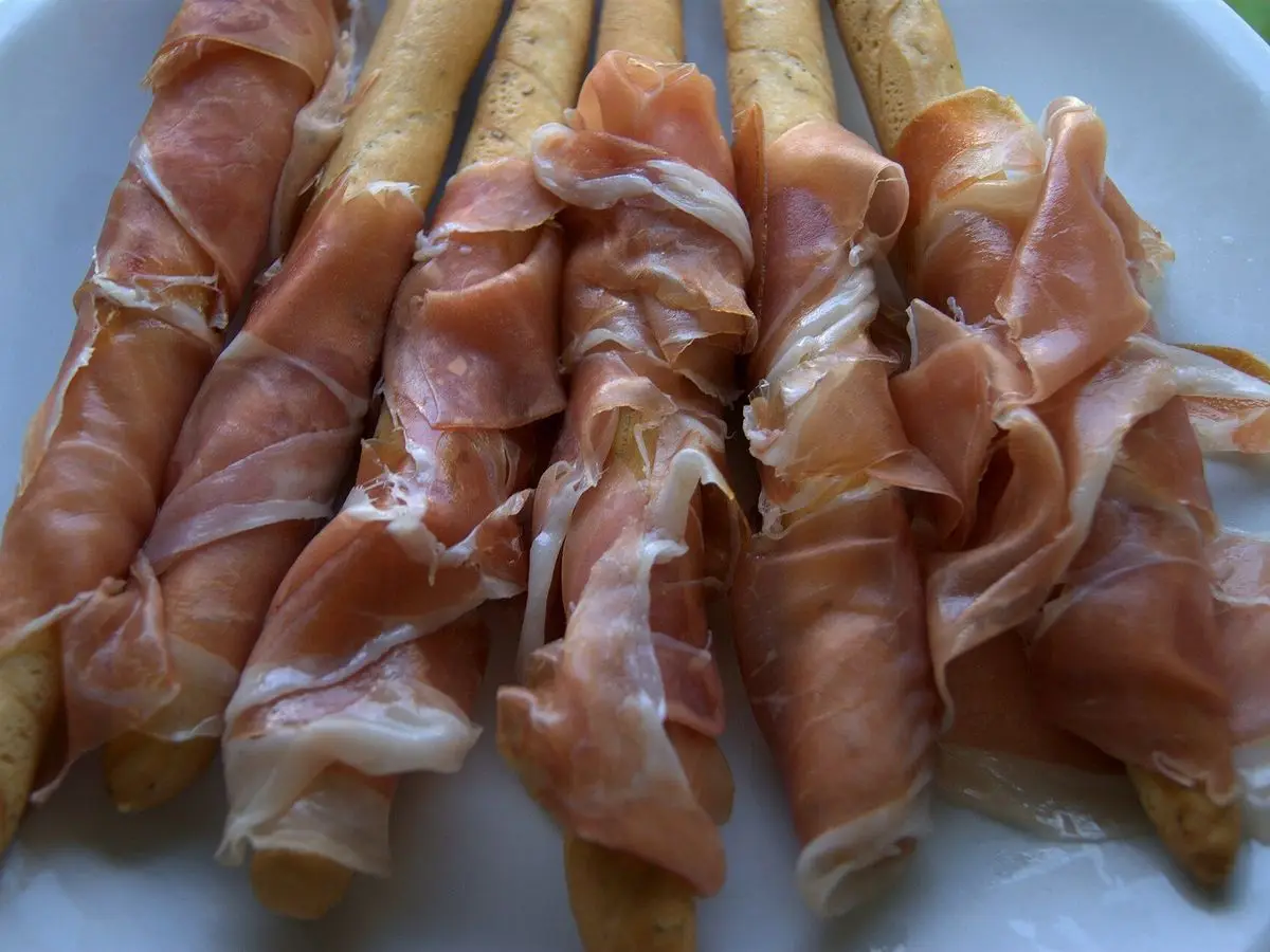 Grisines envueltos en lonchas de jamón curado sobre un plato blanco