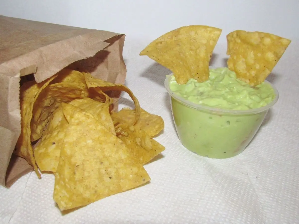 Cuenco de guacamole verde con totopos de maíz y una bolsa de papel