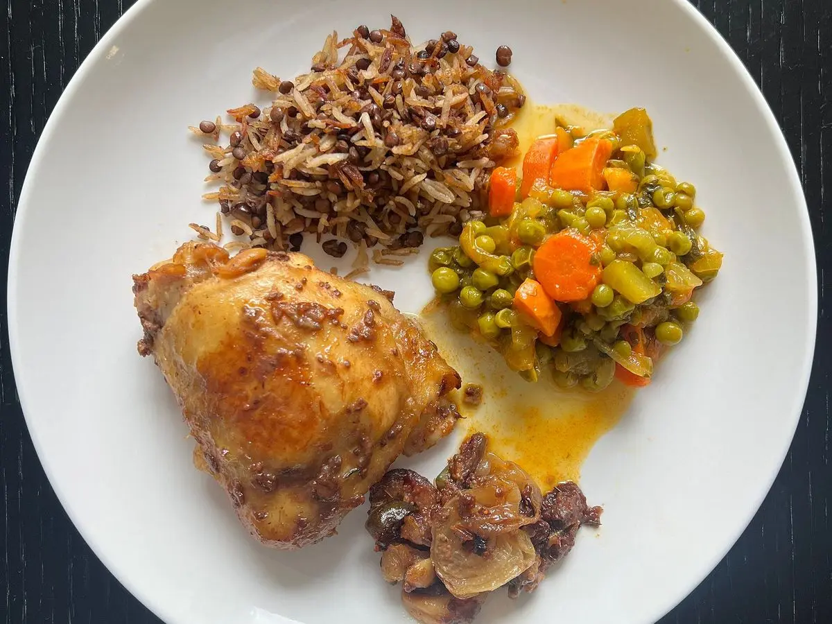 Muslo de pollo asado con guisantes y zanahoria, arroz salvaje y setas en un plato blanco