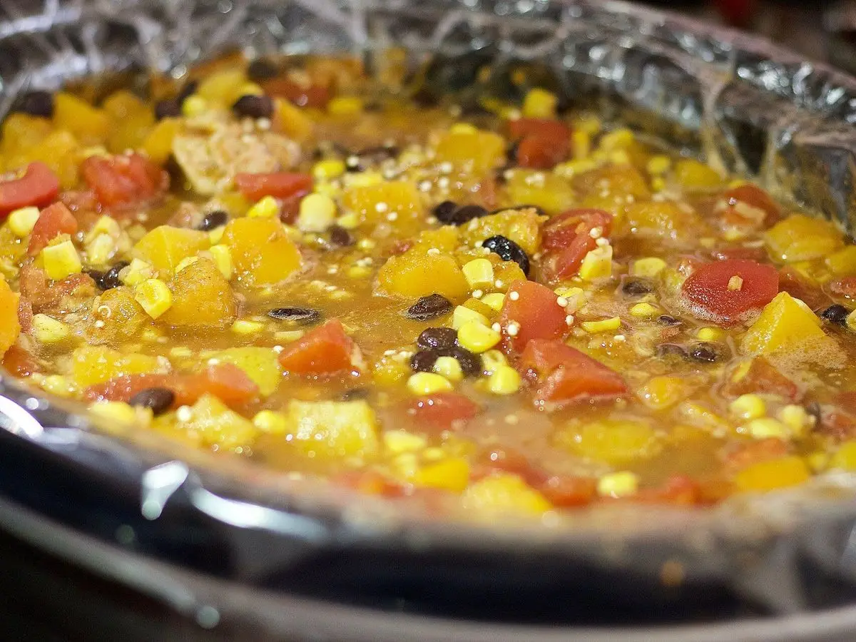 Guiso espeso de quinoa con calabaza, maíz, tomate y alubias negras en una olla de cocción lenta
