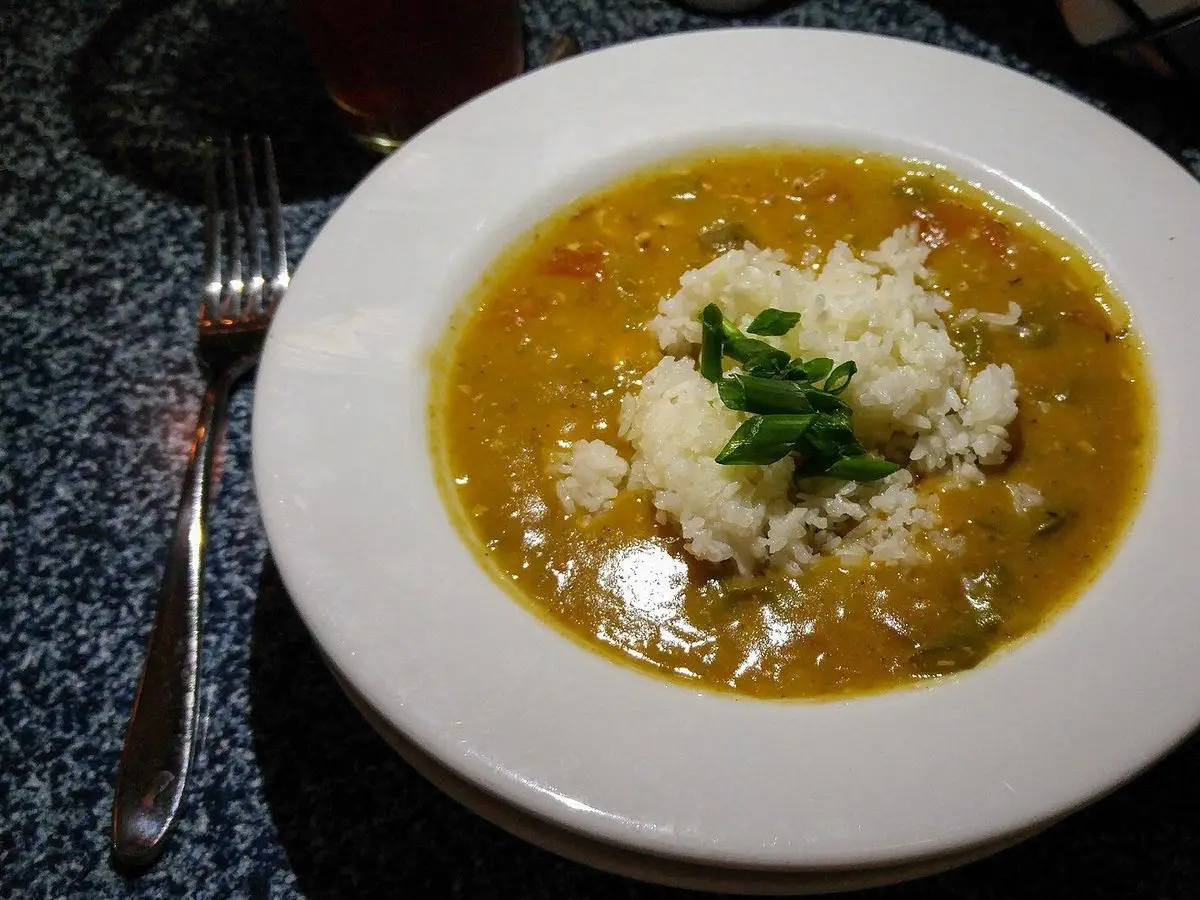 Plato hondo blanco de gumbo cajún con caldo especiado, arroz blanco en el centro y cebollino