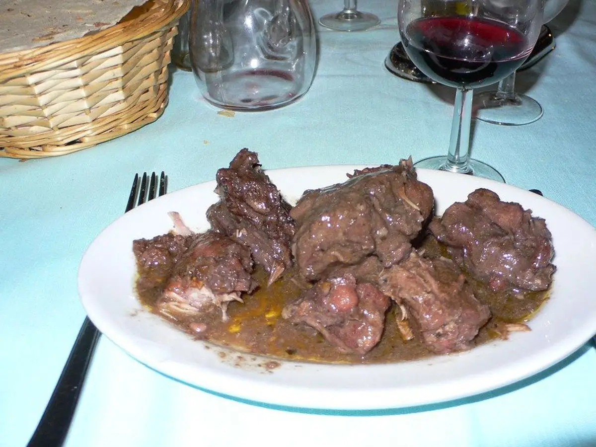 Plato blanco con trozos de carne de conejo guisada en salsa oscura