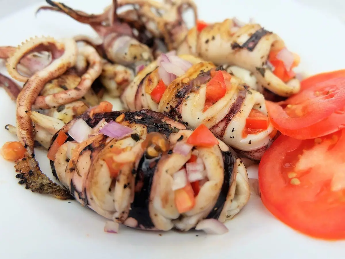Calamares cocinados en rodajas con cebolla y tomate picado, acompañados de rodajas de tomate