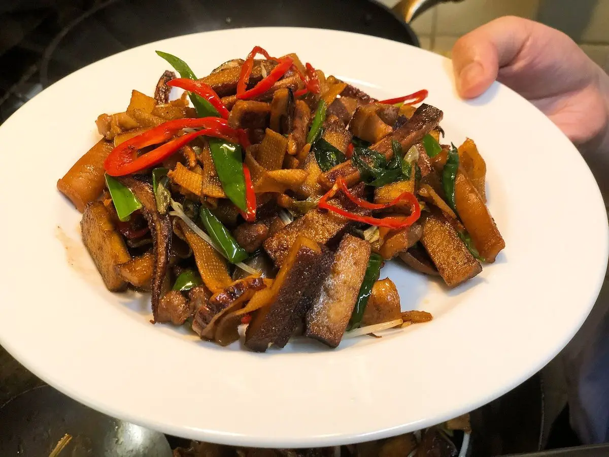 Plato blanco de salteado hakka taiwanés con tiras de calamar, cerdo y tofu, cebolleta y guindilla roja