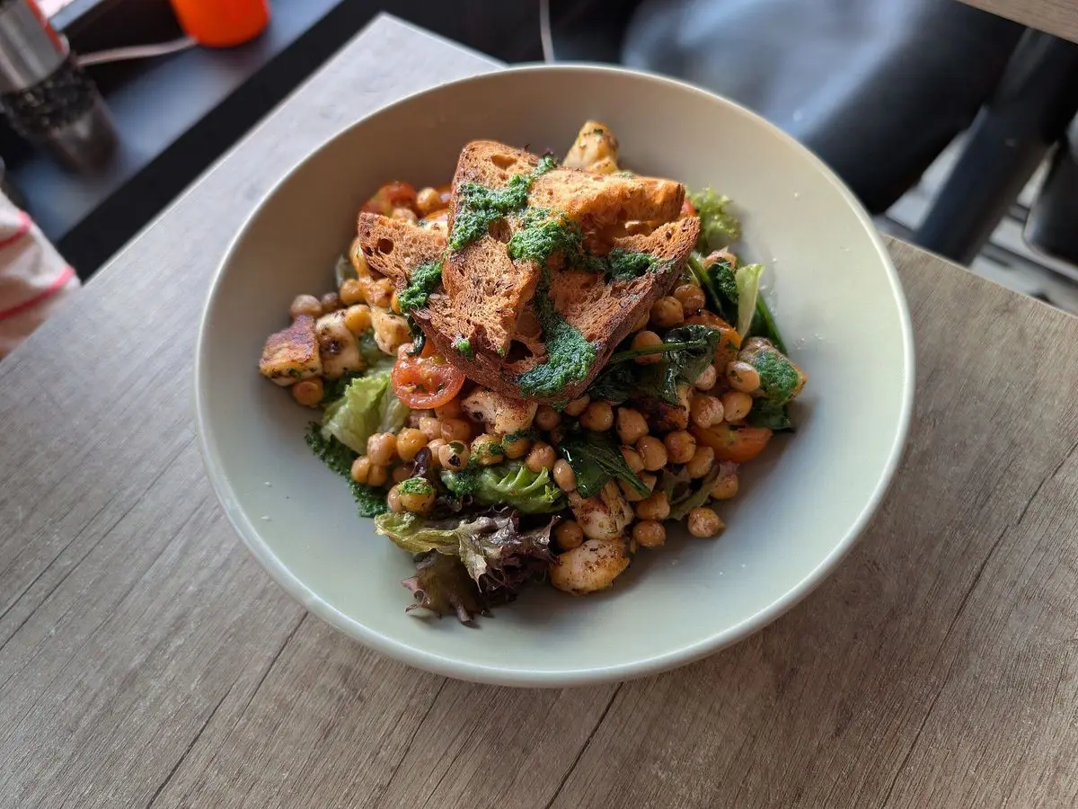 Cuenco con ensalada de garbanzos crujientes, halloumi dorado, tomate y hierbas frescas sobre una mesa de madera