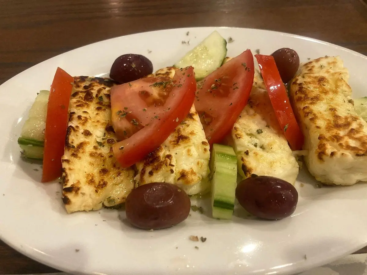 Queso halloumi a la plancha con tomate, pepino y aceitunas en un plato blanco