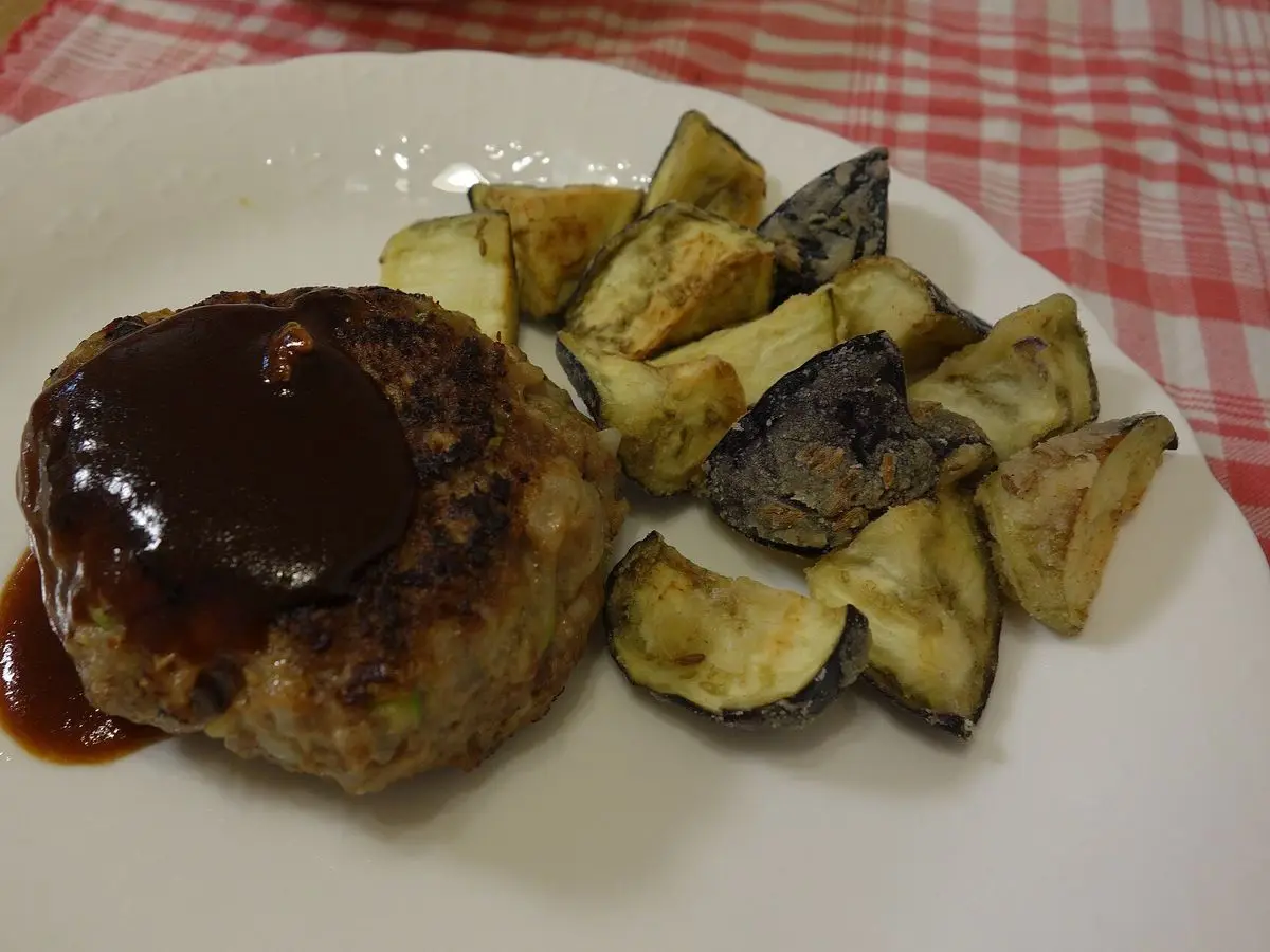 Hamburguesa de carne con salsa oscura y patatas asadas en un plato blanco