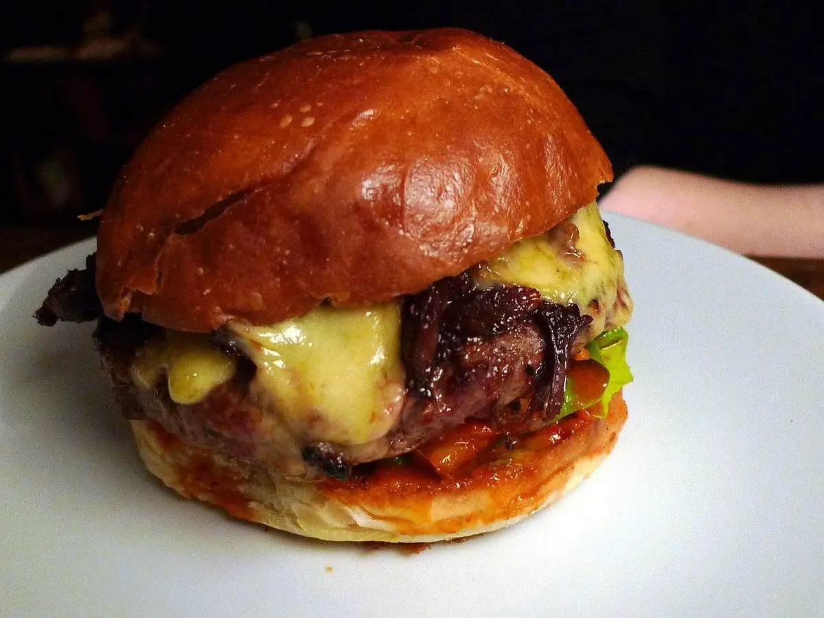 Hamburguesa con kimchi y queso fundido en pan brillante sobre un plato blanco