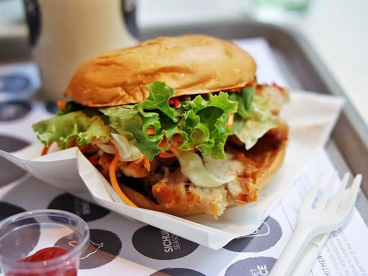 Hamburguesa con lechuga y salsa en pan redondo sobre papel, en una bandeja