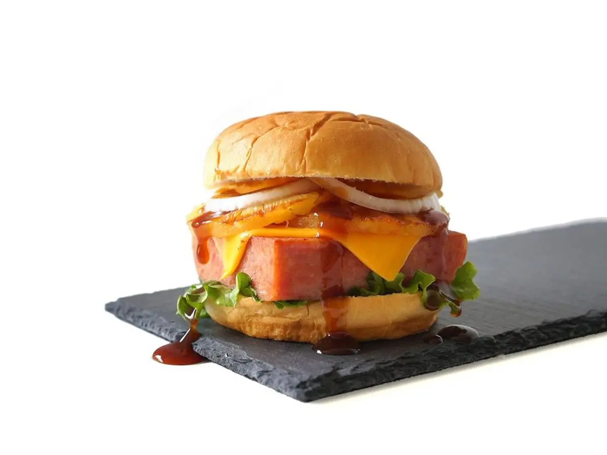 Hamburguesa con jamón, queso fundido y aro de piña sobre una pizarra