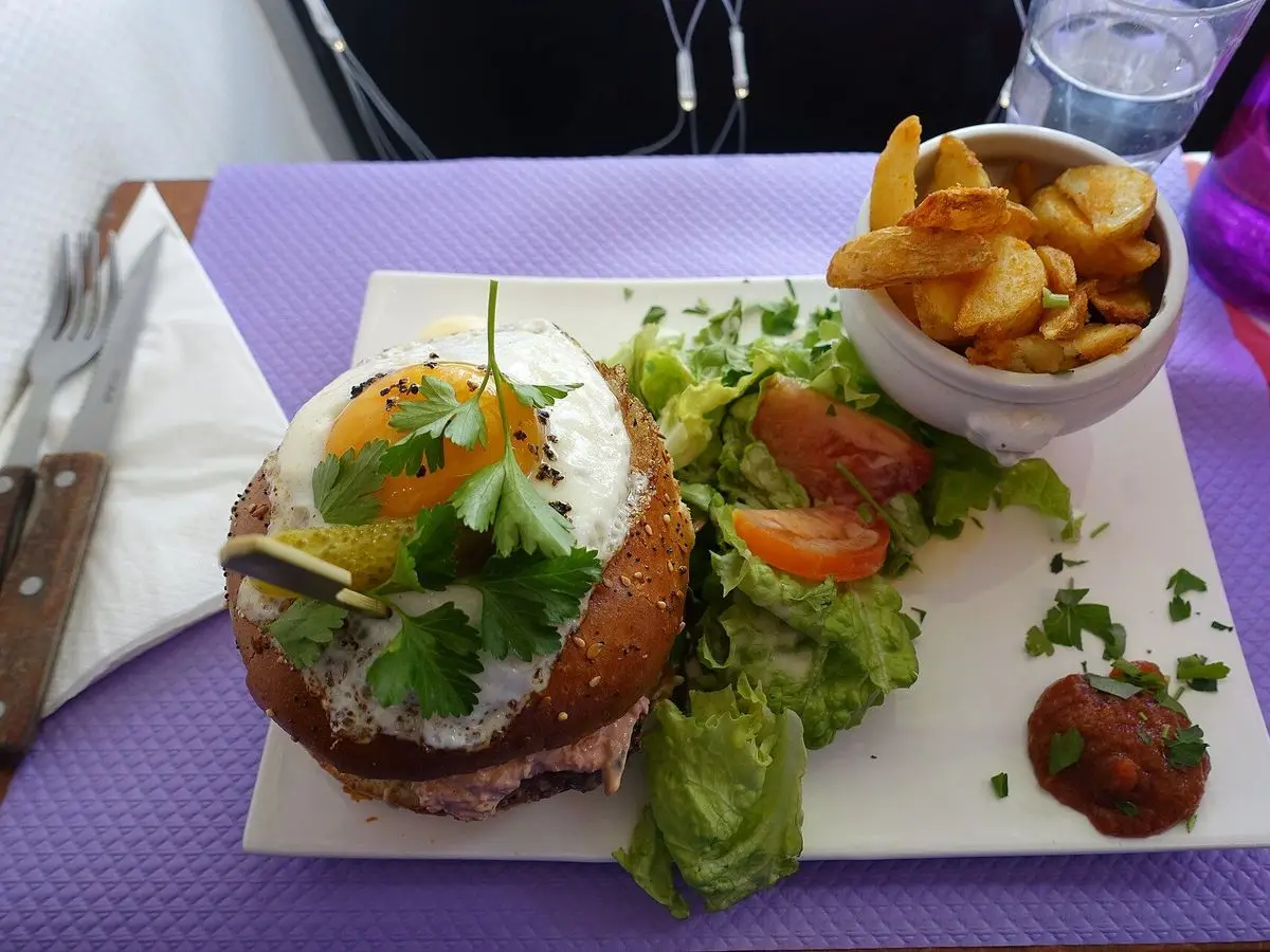 Hamburguesa con huevo frito encima, ensalada de lechuga y tomate y patatas en un plato cuadrado