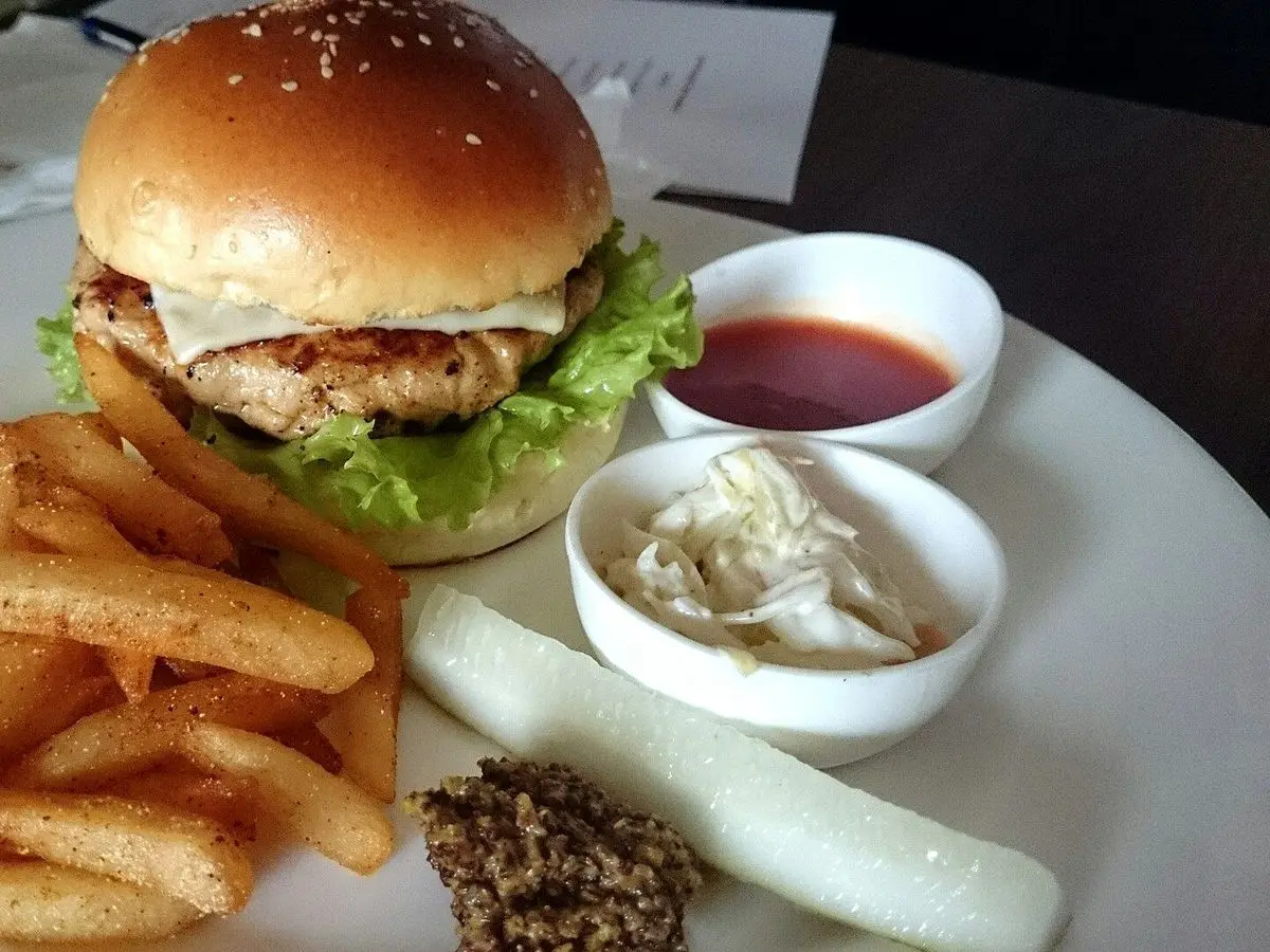 Hamburguesa de pollo con lechuga en pan de semillas, patatas fritas y salsas en pequeños cuencos
