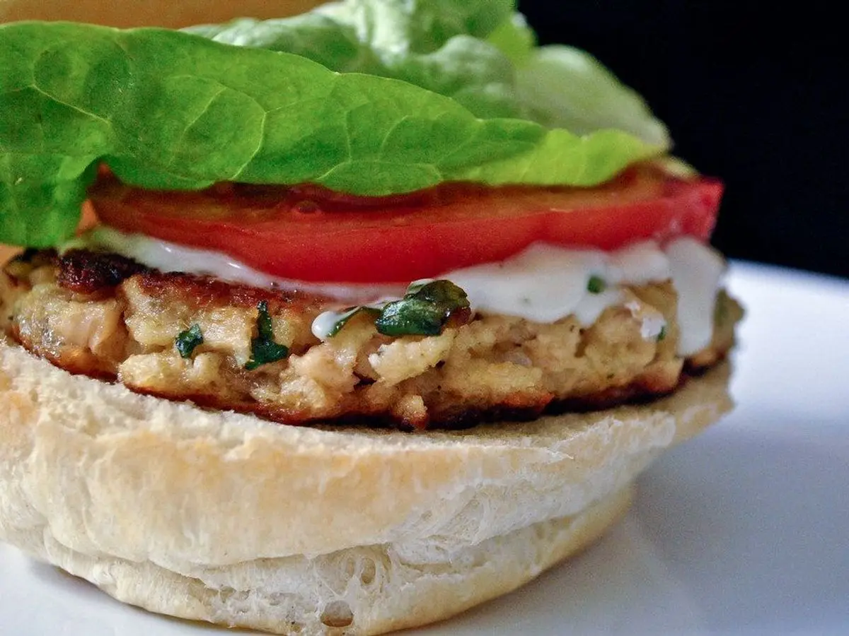 Hamburguesa de salmón con lechuga, tomate y salsa blanca en un pan redondo
