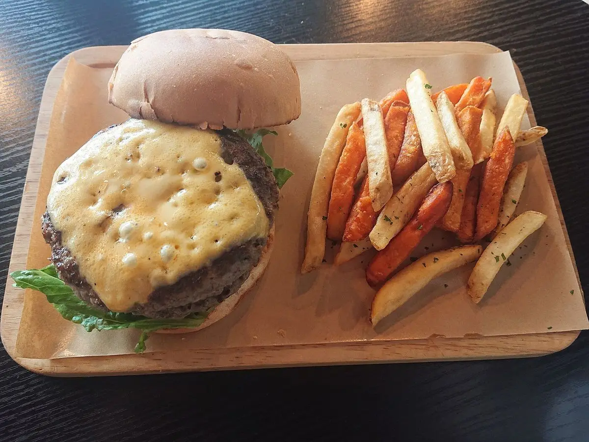 Hamburguesa de ternera con queso en pan junto a patatas fritas y de boniato en una bandeja