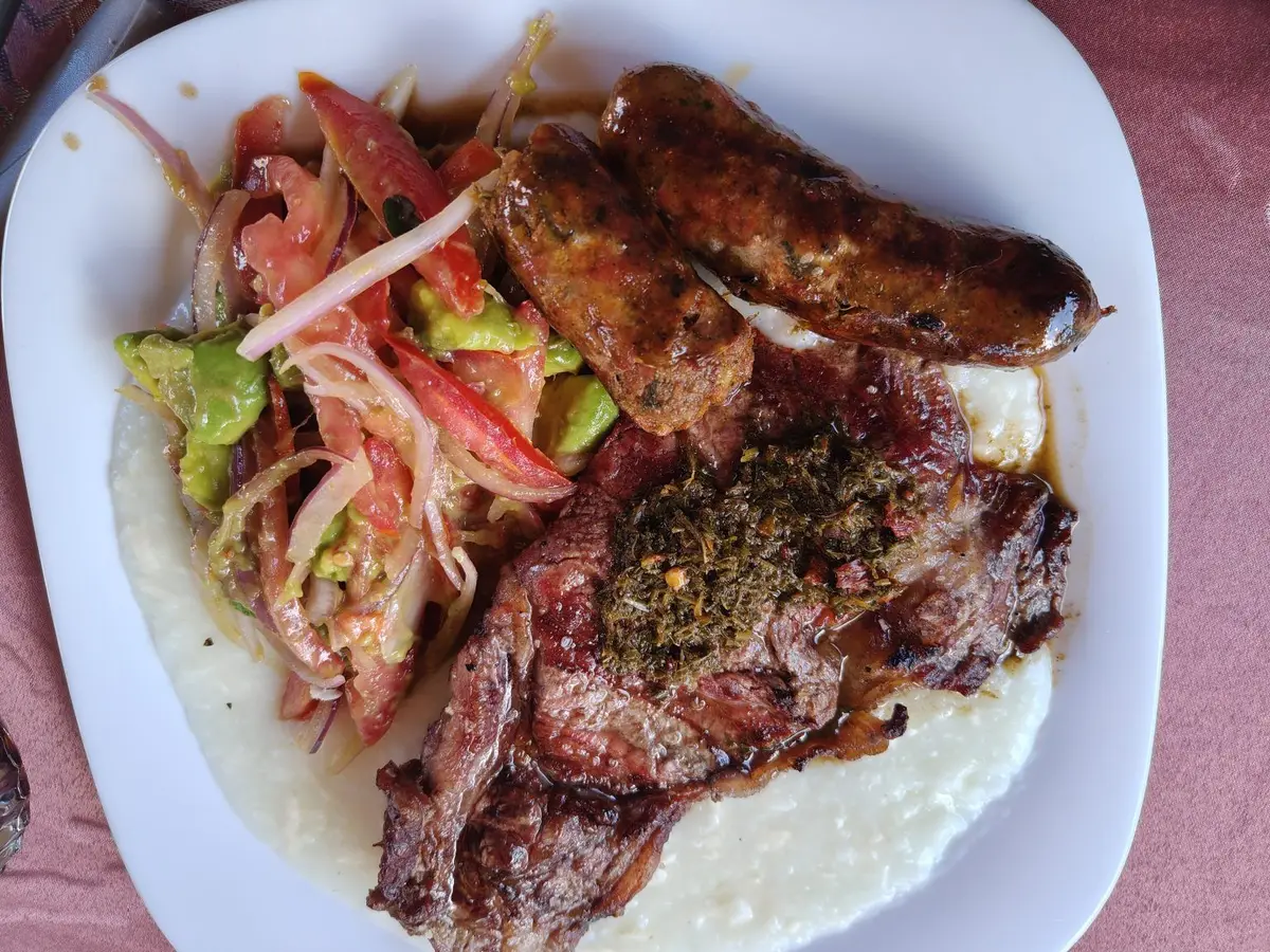 Carne a la plancha y salchichas con ensalada de tomate, cebolla y aguacate