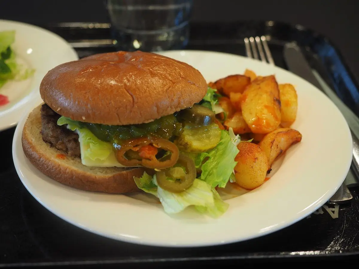 Hamburguesa con lechuga y tomate acompañada de patatas gajo en un plato blanco