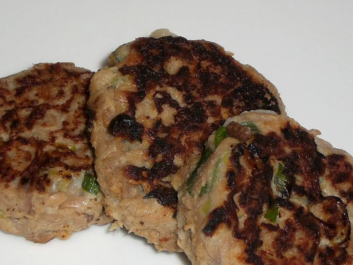 Tres hamburguesas caseras de atún doradas a la plancha, con trocitos de cebolleta, sobre fondo blanco