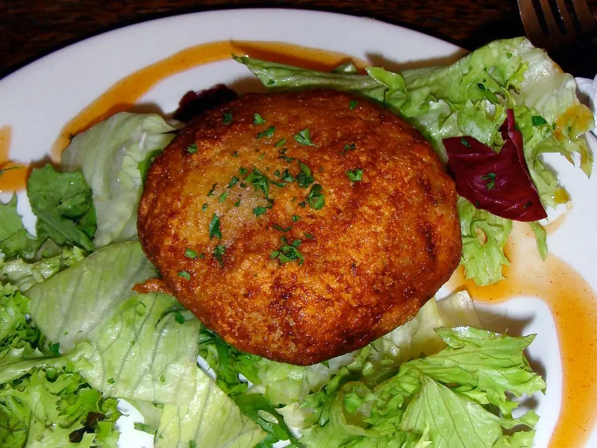 Hamburguesa de pescado dorada sobre cama de ensalada de lechugas variadas y salsa anaranjada