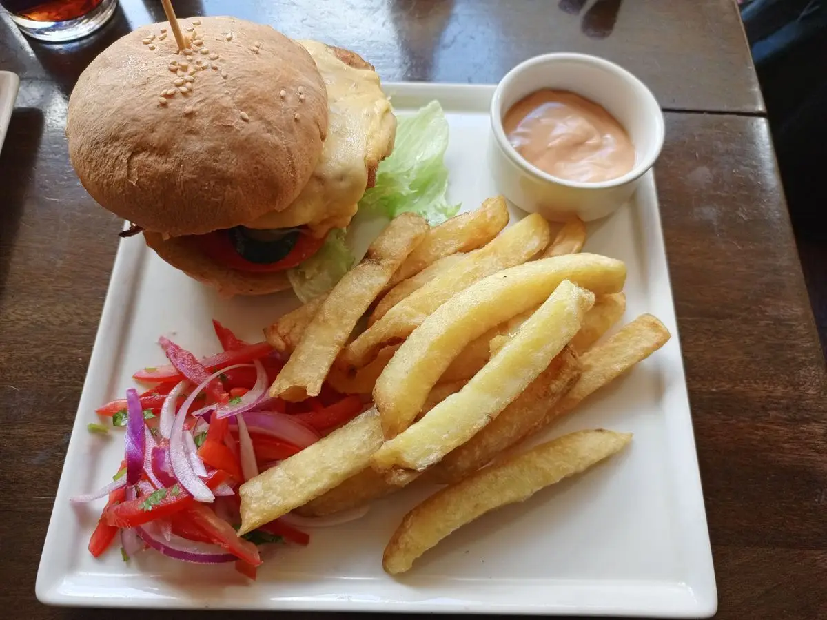 Hamburguesa casera con lechuga y queso, patatas, ensalada de tomate y cebolla y una salsa