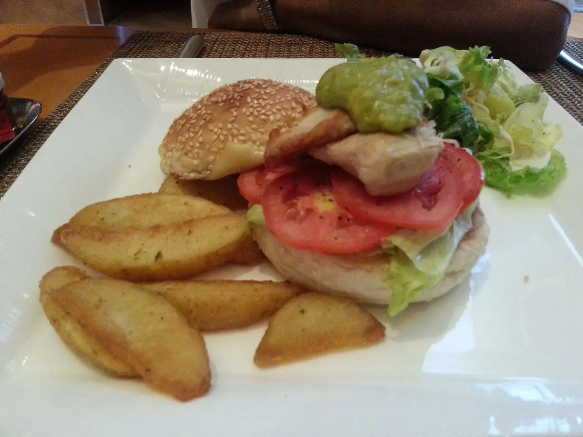 Hamburguesa de pollo con tomate y lechuga acompañada de patatas gajo en un plato blanco