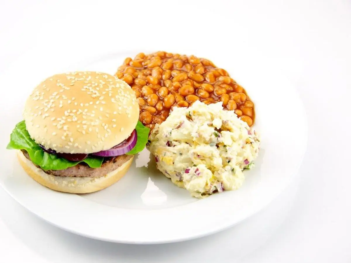 Hamburguesa de pavo en pan con lechuga y cebolla morada, con alubias y ensalada de patata al lado