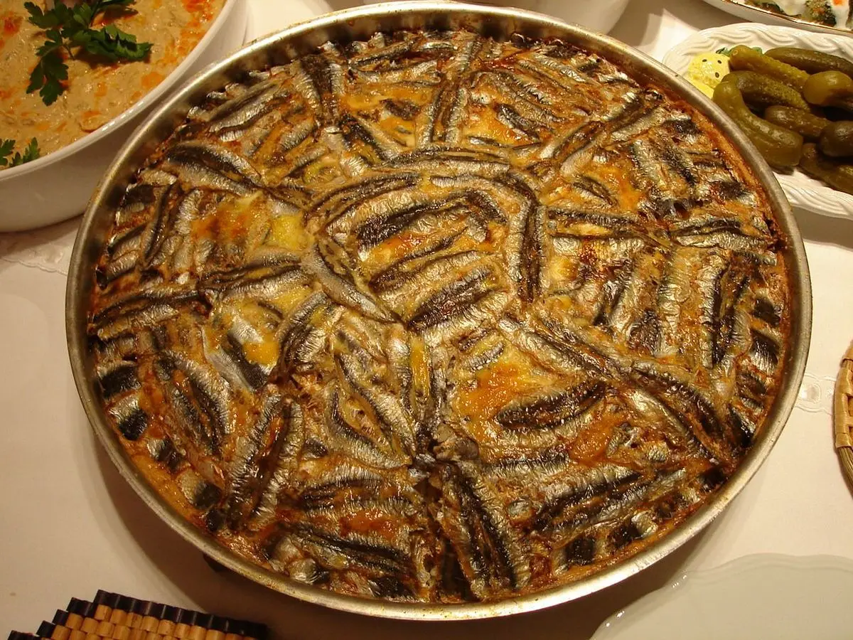 Bandeja redonda de arroz al horno cubierta con boquerones colocados en círculos concéntricos