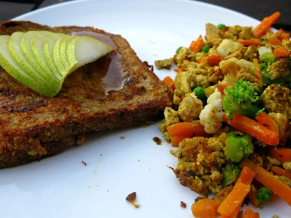Plato con salteado de tofu y verduras como zanahoria y brócoli junto a una tostada con rodajas de fruta